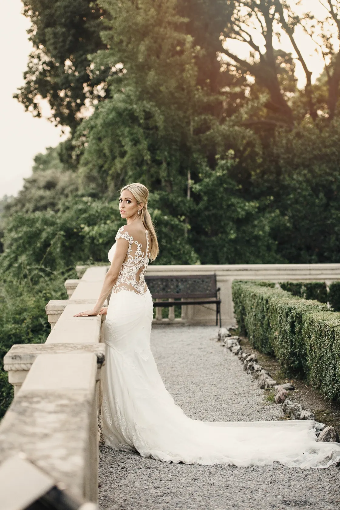 A bride in a backless gown at a stone balustrade in late golden light