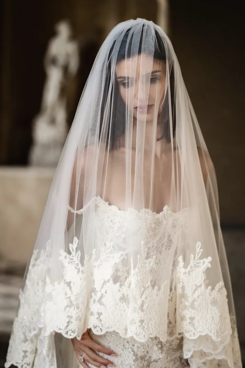 Portrait of a bride beneath a sheer embroidered veil, eyes lowered