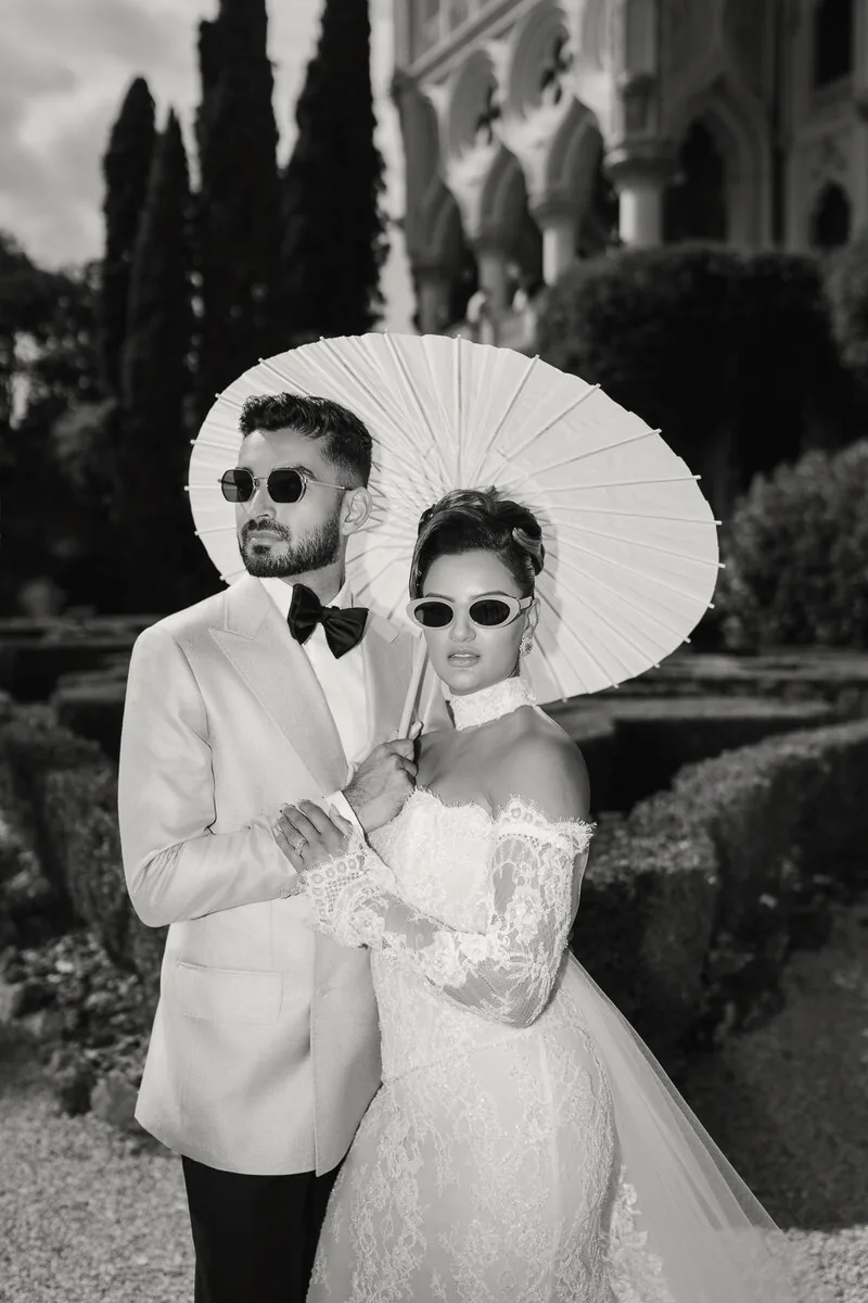 Black and white portrait of a couple in sunglasses beneath a parasol in a villa garden