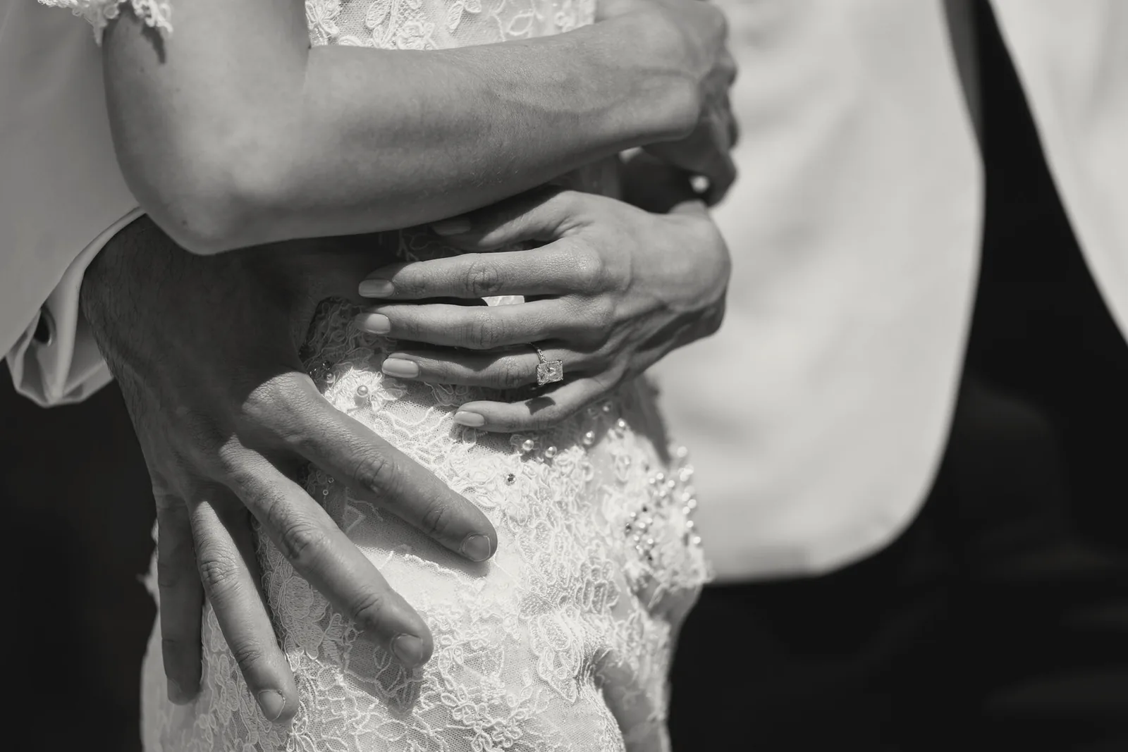 Black and white close-up of a groom's hands holding the bride at the waist