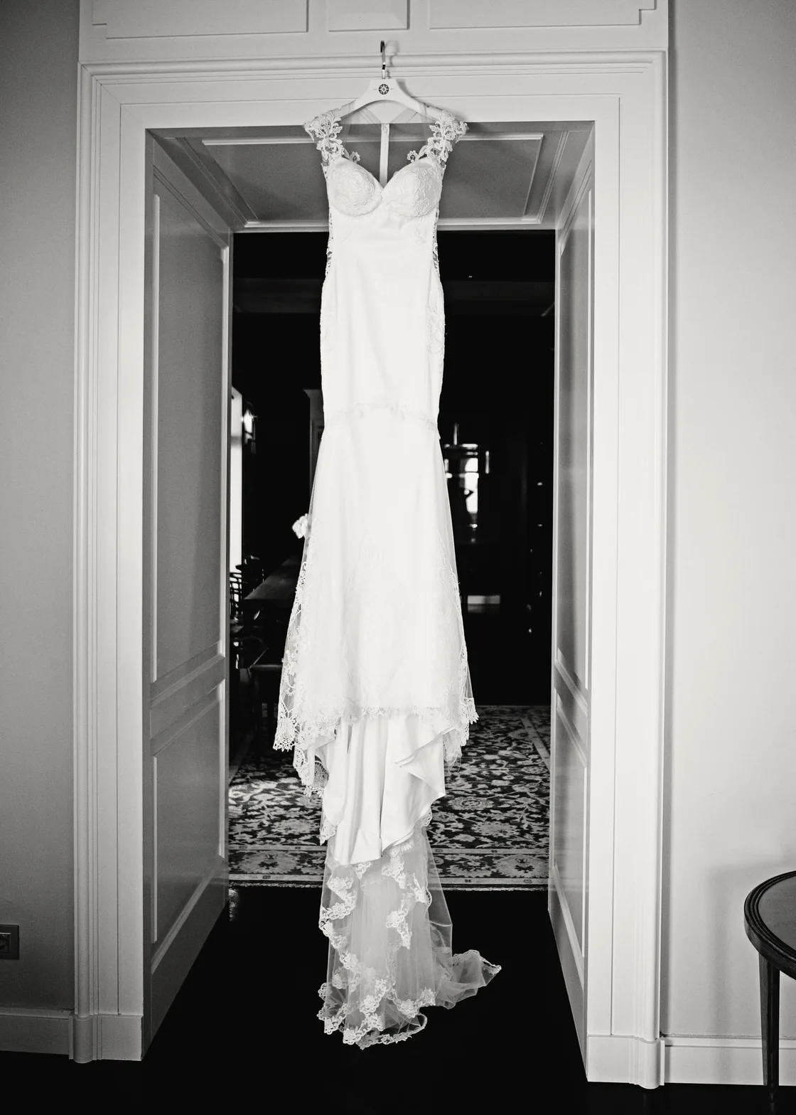 Black and white photo of a wedding gown hanging in a tall doorway