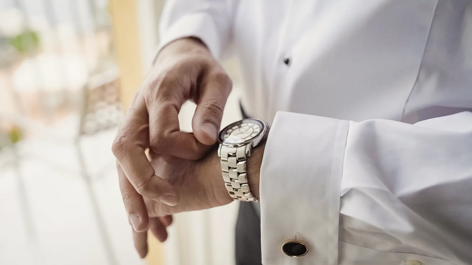 Close-up of a groom fastening his watch over a crisp white shirt cuff