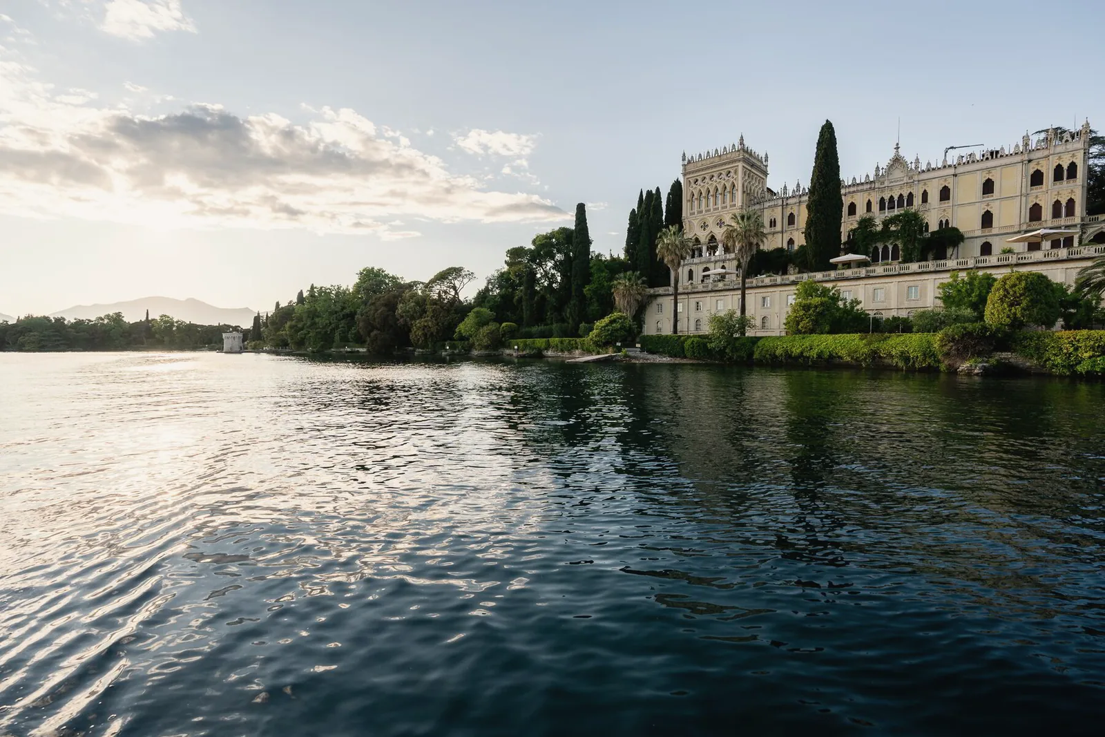 A neo-Gothic villa among cypress trees on an island, seen across calm water