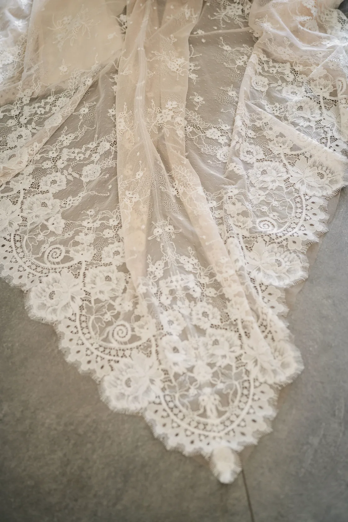 Detail of a lace bridal train spread across a stone floor