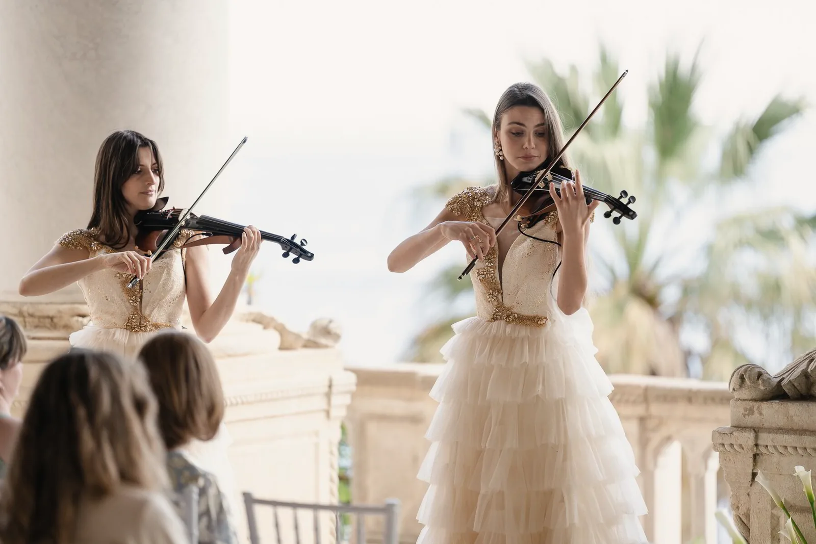 Two violinists play on a sunlit terrace before the ceremony